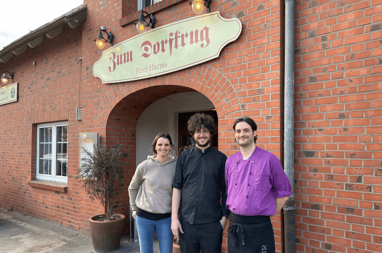 Drei Personen posieren vor dem Dorfkrug Harms.