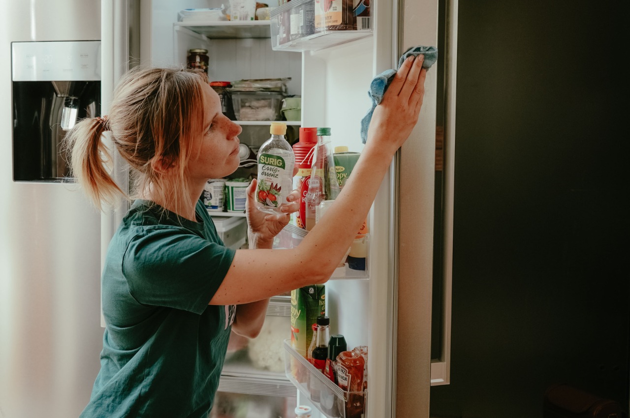 Person steht vor geöffnetem Kühlschrank und reinigt die Tür mit einem Tuch