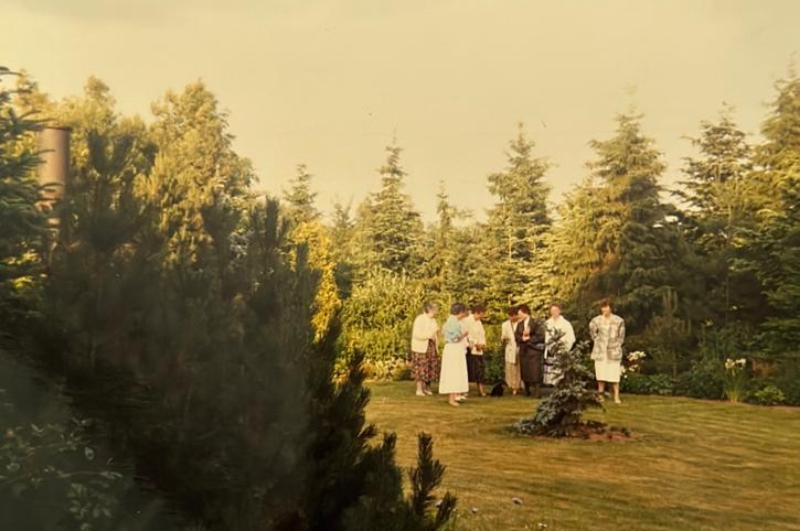 Personengruppe steht im Garten zwischen Tannenbäumen